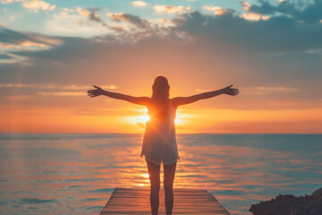 Woman with open arms under the sunrise at seaside wellness concept.