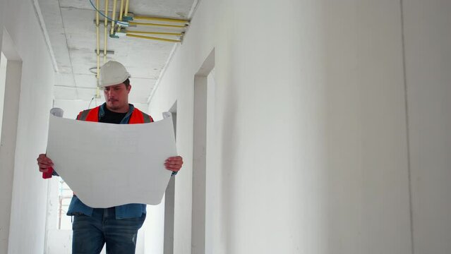 Architect or engineer wearing hardhat looking blueprint for inspection and planning construction at construction site, contractor or builder walking examining and checking project development house.