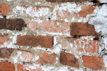 Fragment of a red brick wall. Part of the white plaster on the wall had fallen off. View of a plastered brick wall.