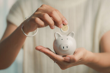 Person deposits a coin into a piggy bank, demonstrating the act of saving money and making a...