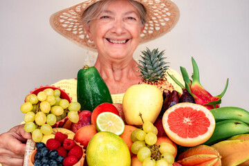 Defocused happy senior woman in straw hat holding basket full of fresh exotic fruit, healthy lifestyle concept
