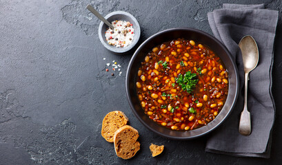 Bean soup in a black bowl. Grey background. Copy space. Top view.
