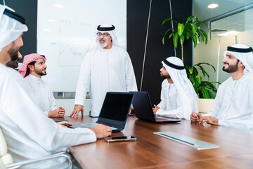 Group of corporate arab businessmen meeting in the office - Business people wearing emirati clothing  working in the office
