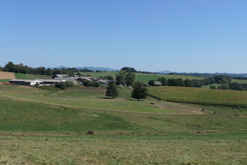Obraz premium In the French countryside, rolling hills stretch across the landscape, adorned with vibrant greenery during the summer. A charming farm, complete with a rustic barn.