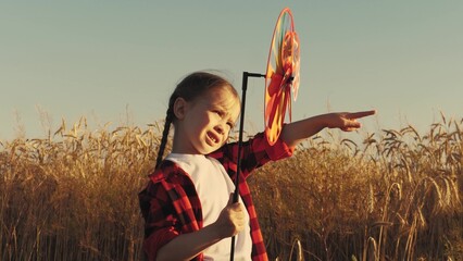 Happy little girl runs across field park sunset, holding toy windmill hands. happy kid child enjoys...