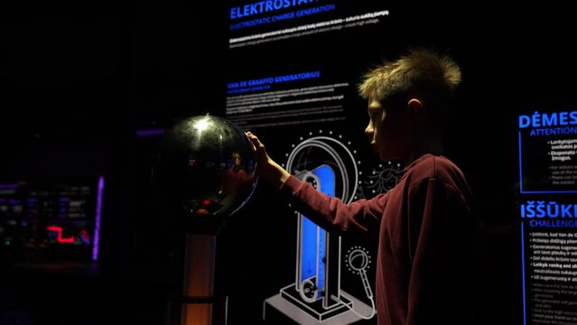 Generation of electrostatic charge. Close-up camera shot of young boy creating static electricity. Smart boy with school uniform makes his hair static at the museum exhibition.