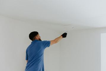 A young oriental man paints the ceiling with a roller.