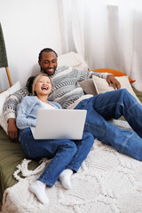 Smiling young interracial couple relaxing with laptop on bed at home