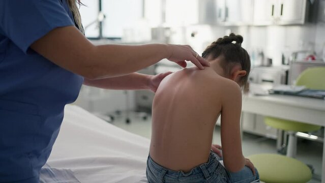 Orthopedist examines the spine, posture, and spinal deformities of little girl. Girl visiting paediatrician for annual preventive exam. Concept of preventive health care for children.