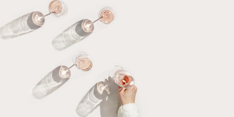 Rose wineglass in woman hand, Minimal style flat lay. Holiday aesthetic still life photo, top view wine glasses at sunlight, sun shadow, monochrome beige peach pink pastel color, copyspace
