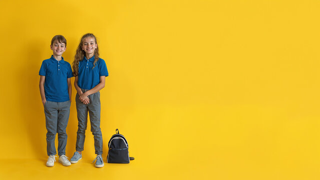 deux &eacute;coliers en uniforme scolaire, polo bleu et pantalon gris - fond jaune