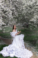 Spring sexy fantasy woman sits on branch of green tree blooming sakura flowers garden. Medieval girl vintage lady. pink silk fly in wind dress. fairy tale image art photo. Brunette long hair cute face