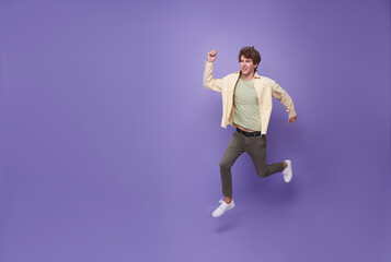 Full length man running jumping in air isolated on purple copy space background. Cool man joyful...