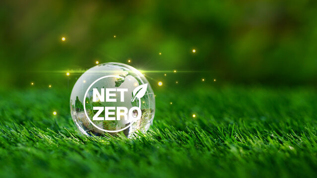 Net Zero text on glass earth globe crystal over green grass in the nature garden background. Environment business management target concept, goal Eco environment friendly.Carbon neutral.