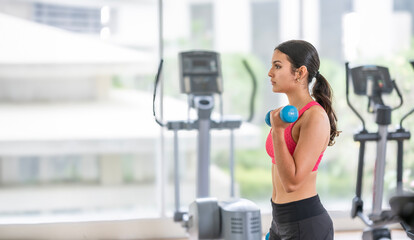 Confident teenage girl in activewear performs a bicep curl with a dumbbell, emphasizing strength...