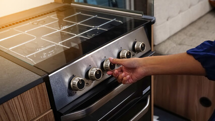Woman hand turning switch knob on gas stove for opening or closing modern electric oven prepare to...