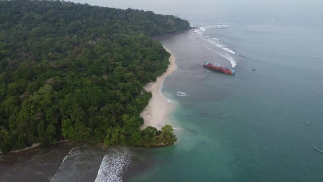 Abandoned ship at the sea near seashore with trees all around. Boats in the ocean aerial view. Pasir Putih, Pangandaran beach
