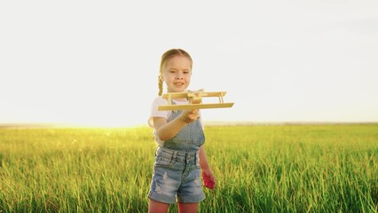 Happy child, girl playing with toy airplane on summer field. Kid holds toy airplane in his hand. Happy family is playing in park. Little Daughter dreams of flying. Carefree kid playing outdoors