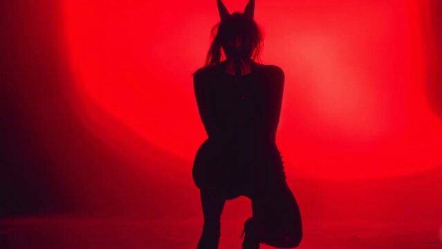 Beautiful sexy demon girl posing at photo studio. Red light background. Female devil with horns. Evil beauty. Pretty Asian model. Young fashionable stylish woman. Attractive sensual monster.