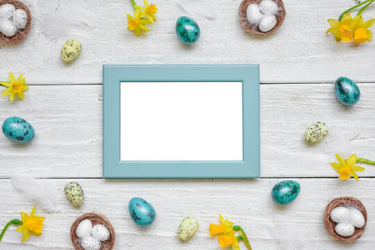 Easter picture photo frame with spring yellow Narcissus flowers and easter colorful eggs on white wooden background. Mock up. Flat lay. Top view with copy space