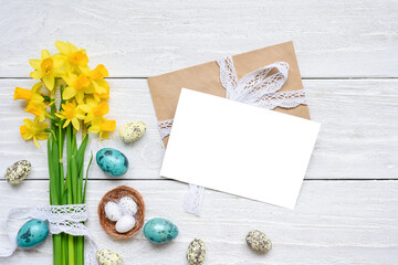 Easter greeting card with spring yellow Narcissus flowers and easter colorful eggs on white wooden background. Flat lay. Mock up. Top view with copy space