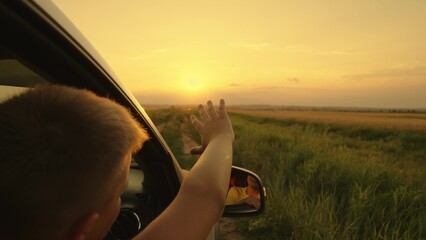 Happy teenager guy rides in a car, waving his hand out the car window. Road travel concept. The boy...