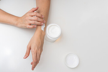 Applying White Cream to the Forearm. A hand gently applies white cream to the forearm from a pot....