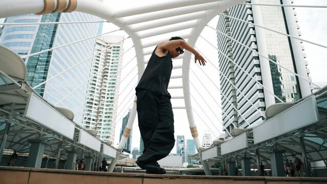Low angle camera of professional street dancer practice b-boy dance. Young attractive funny hipster moving to hip-hop music while performance break dance at urban city. Outdoor sport 2024. Sprightly.