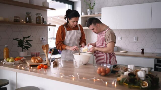 Young man with Down syndrome preparig dough for cookies with his mom at home. Everyday routine for man with Down syndrome.