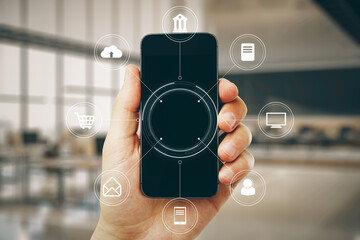 Close up of hand holding smartphone with creative round digital interface with various icons on blurry office interior background. Digital transformation, online banking, shopping and storage concept.