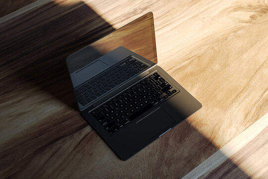 Modern laptop with blank screen placed on a wooden floor, sunlit room, mockup for design presentation. 3D Rendering