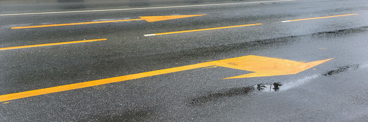 A wet road with yellow arrows on the asphalt.