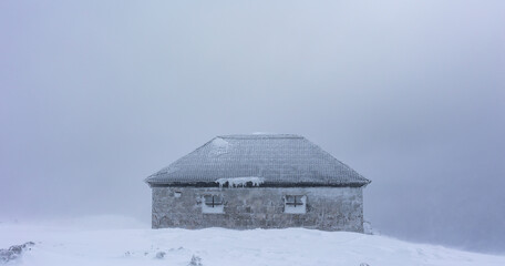 Dom Slaski mountain shelter belod Mount Sniezka. Hard weather conditions in the mountains. Buildings covered in ice. Photo taken on a cloudy winter day