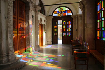 Fototapeta na wymiar Entrada a una iglesia con una puerta de fondo y ventanas con vidrieras, donde entra la luz dejando el reflejo de los colores