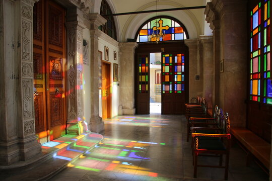 Entrada a una iglesia con una puerta de fondo y ventanas con vidrieras, donde entra la luz dejando el reflejo de los colores