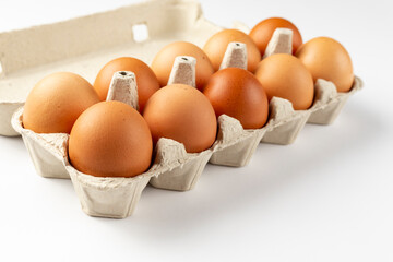 A tray of brown fresh hens eggs on white background. Eco-friendly egg production. Baking ingredients. Organic chicken eggs - fresh from producer. Top view.