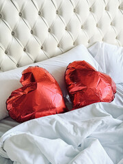 Two red heart-shaped balloons lie on a white bed in a retro bedroom. Wedding day or Valentine’s Day. Vertical image.	