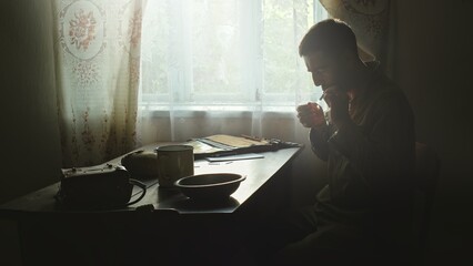 Adult soldier lighting cigarette in rural house. Side view of male scout in soldier uniform sitting...