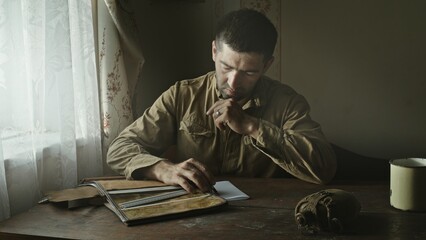A Soviet Army soldier sits at a table in an abandoned farmhouse and looks at a map of the area....