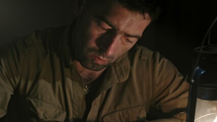 Soldier writing letter to home. Tilt down view of Soviet soldier sitting at table and writing message to home in dim light of oil lantern while taking break during World War II.