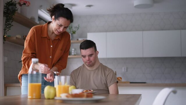 Young man with Down syndrome having breakfast with his mother at home. Morning routine for man with Down syndrome.