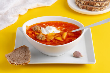 Ukrainian and Russian cuisine. Red borscht. Soup of tomatoes, cabbage and vegetables. Borscht in a white bowl on a yellow background