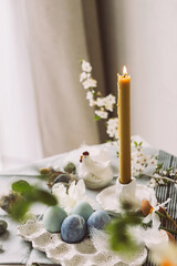 Happy Easter! Stylish easter eggs in tray, cherry blossom and candle on rustic table. Modern natural dyed marble eggs and spring flowers. Easter still life in countryside home