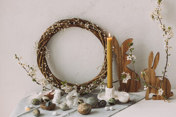 Happy Easter! Stylish easter eggs, wooden bunnies, cherry blossom and candle on rustic table. Modern natural dyed marble eggs and spring flowers. Easter still life decor in countryside home