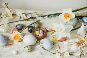 Happy Easter! Stylish easter eggs, bunnies, cherry blossom and daffodils on rustic table. Modern natural dyed eggs and spring flowers. Easter still life decor in countryside home