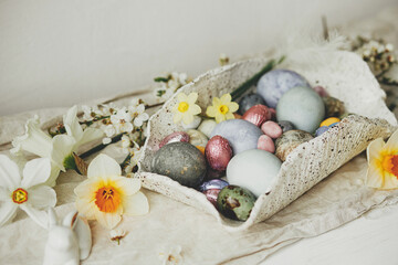 Happy Easter! Stylish easter eggs in modern bowl with cherry blossom and daffodils on rustic table....