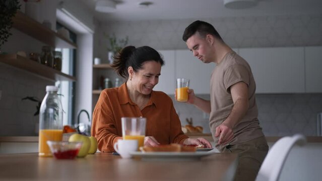 Young man with Down syndrome preparing breakfast with his mother at home. Morning routine for man with Down syndrome.