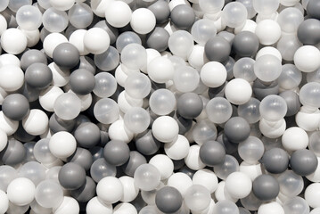 Plastic balls in a dry pool for children, different soft balls gray and white colors background.