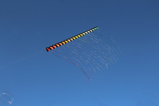 Aquilone composto da tanti piccoli aquiloni colorati con una lunga coda che vola nel cielo blu.