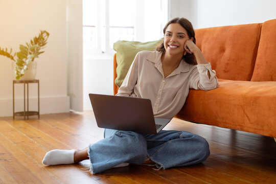 Young woman working on her laptop while sitting on floor at home